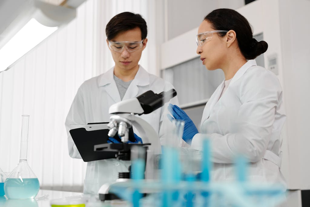 Asian scientists in lab coats discussing research with a microscope in a laboratory setting.