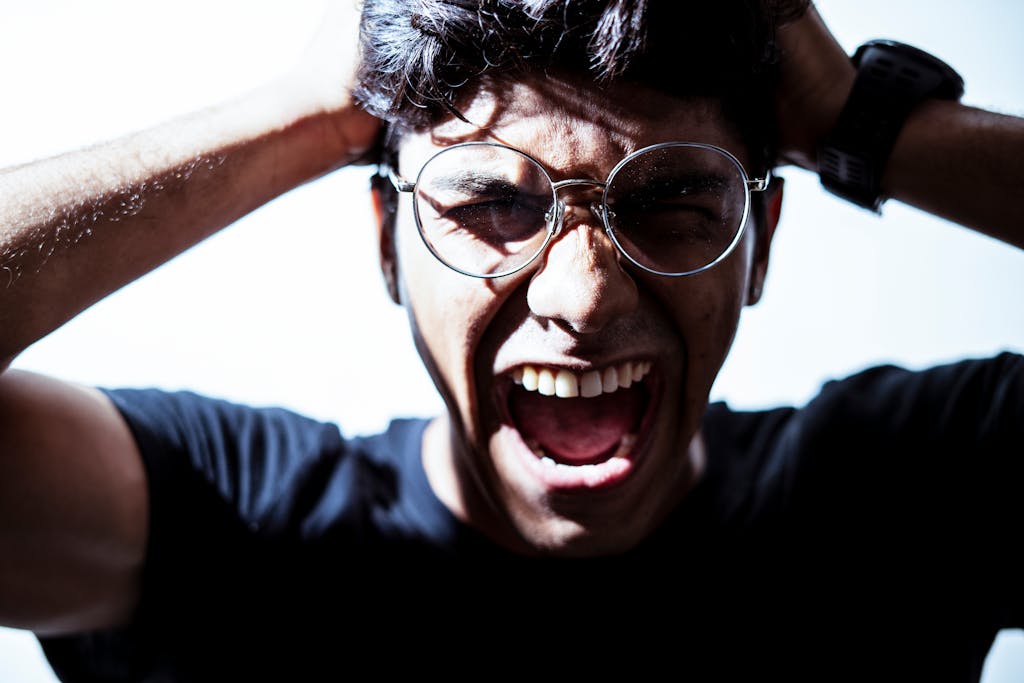 Close-up of a man wearing eyeglasses, expressing intense emotion by shouting.