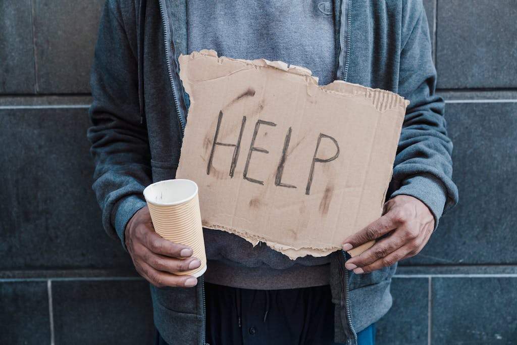 Close-up of a person holding a help sign and paper cup, highlighting social issues.