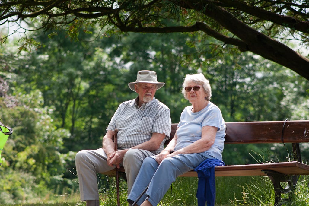 Senior couple sitting on a park bench enjoying a sunny day outdoors.