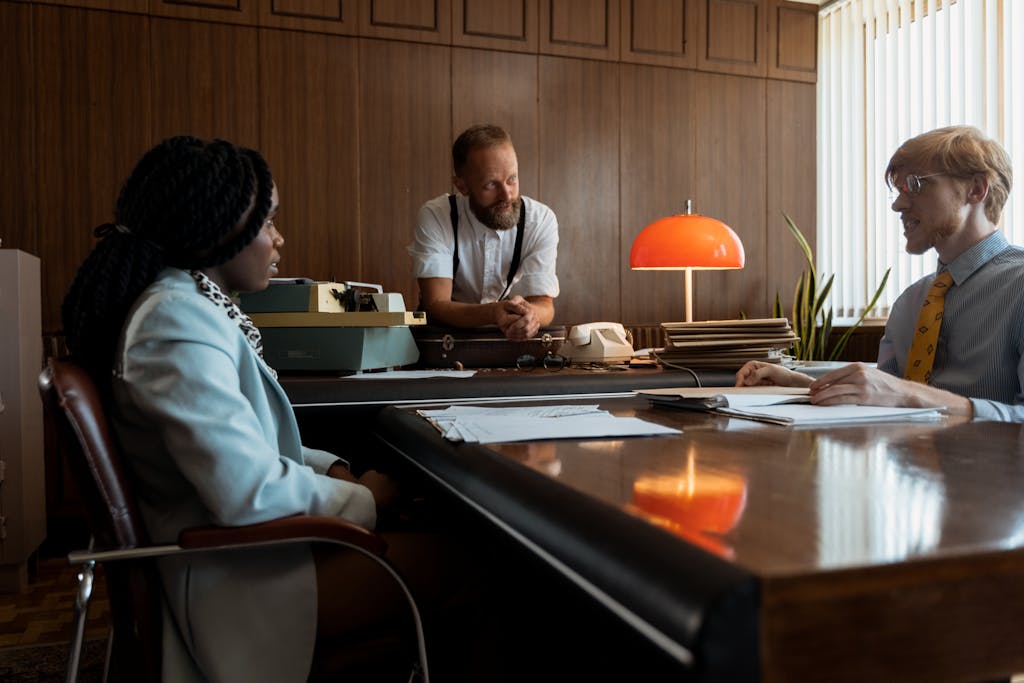 Three colleagues engage in a discussion around a vintage desk in a retro office space.